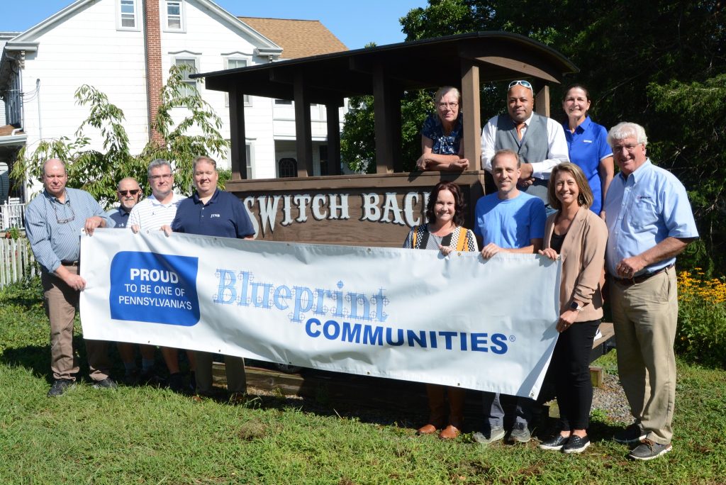 Group of people in front of switchback car with blueprint communities banner