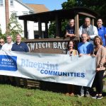 Group of people in front of switchback car with blueprint communities banner